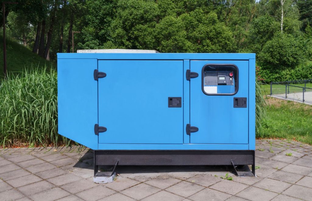 Blue silent diesel generator installed outdoors on a paved platform, surrounded by green grass and trees, showcasing modern backup power equipment.